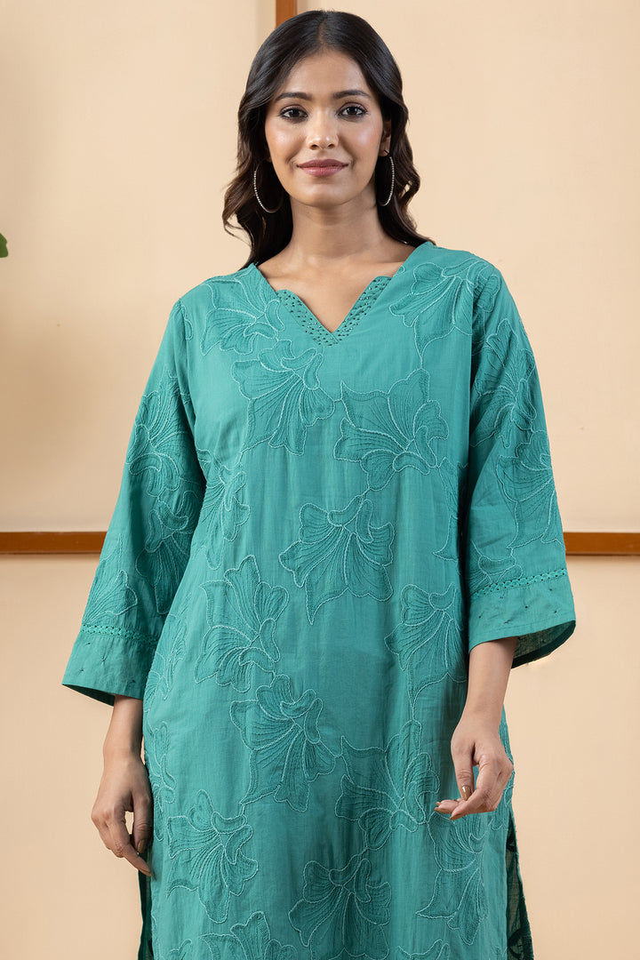 Close-up of delicate embroidery details around the V-neckline on soft green cotton fabric
