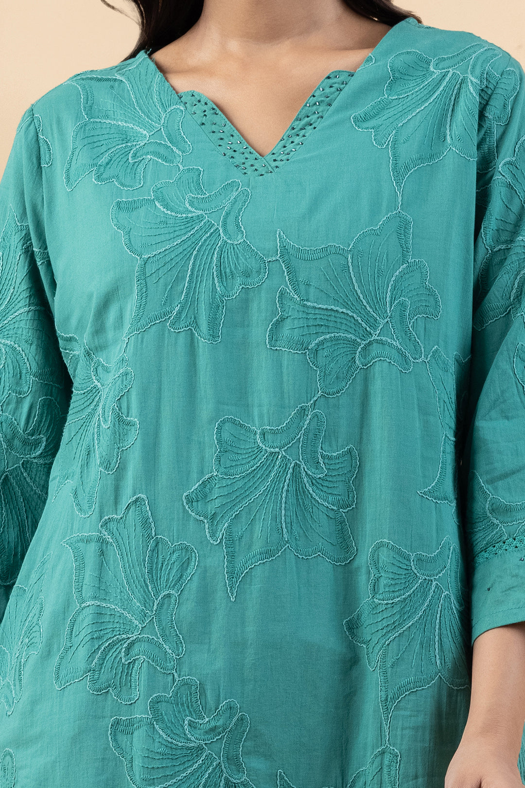 Close-up of delicate embroidery details around the V-neckline on soft green cotton fabric